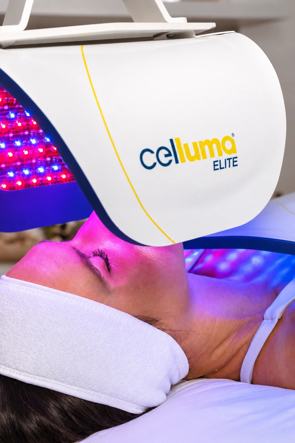 女士在 Celluma ELITE 面板下接受面部光療的近照,可見儀器標誌及亮起的 LED