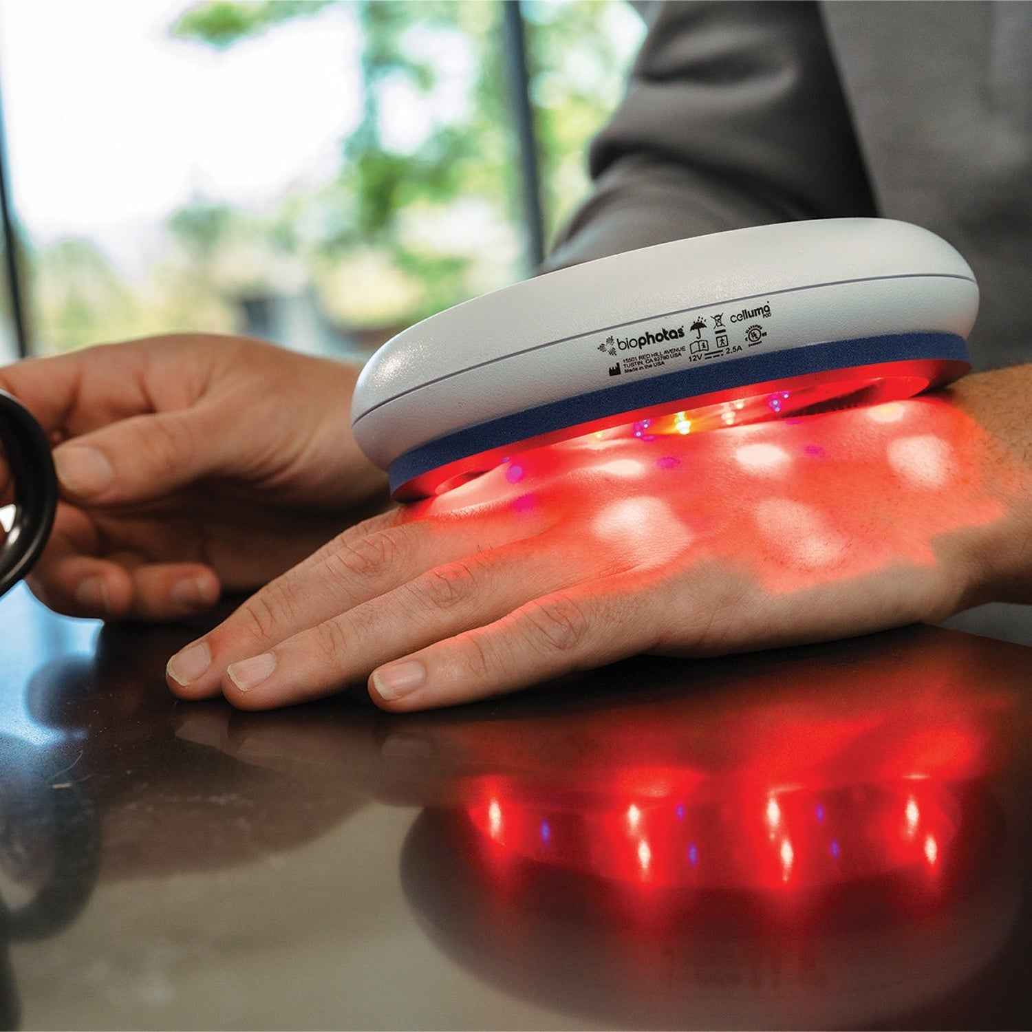 A woman using Celluma POD LED red light therapy to treat pain on her back of her hand.