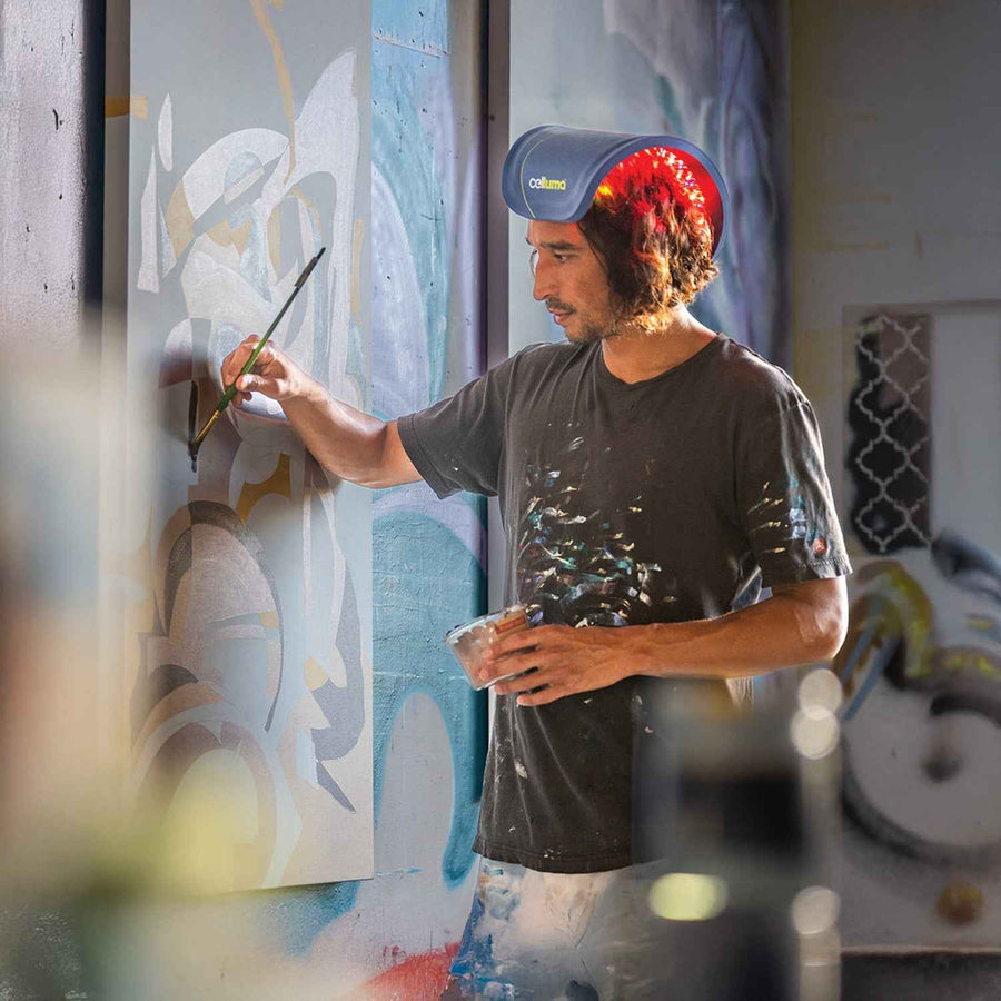Man painting a mural with a spray can in an art studio while using red light therapy for hair growth.