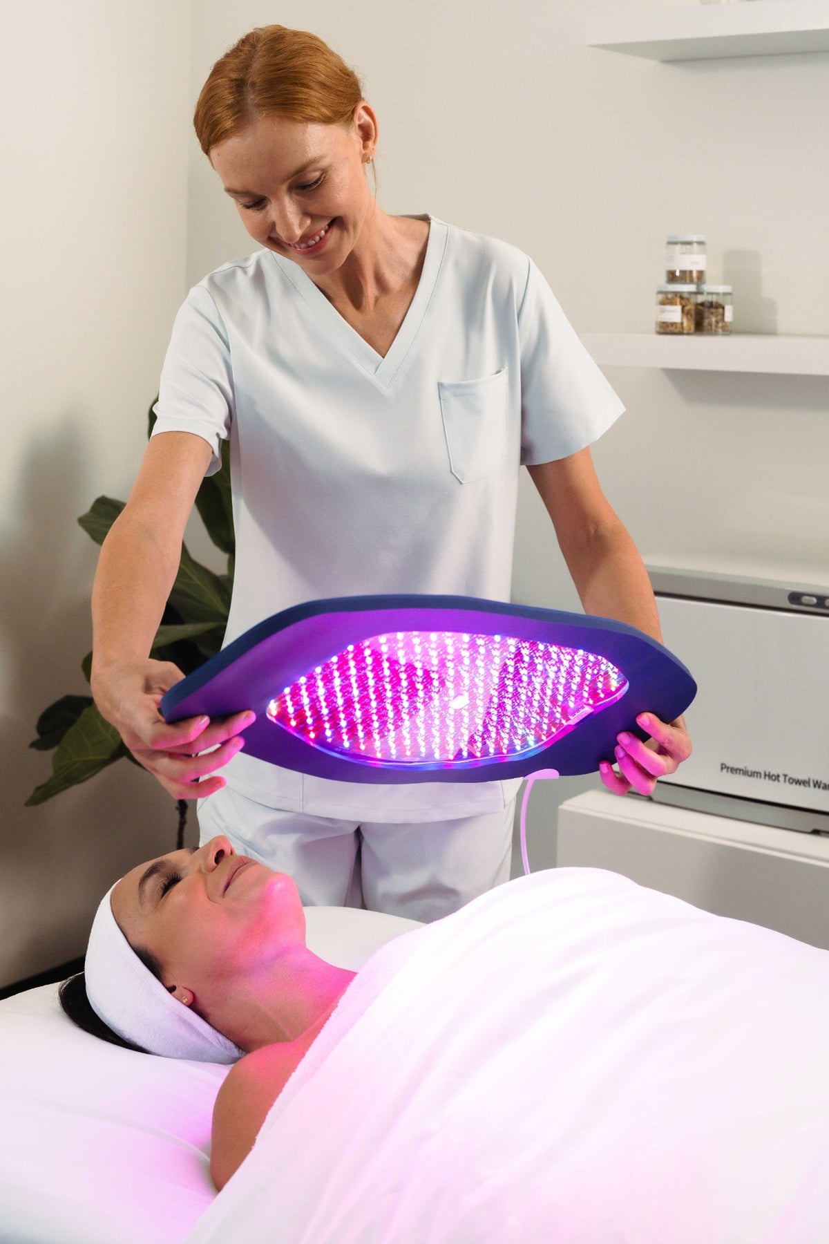Practitioner positioning an illuminated Celluma panel above a reclining client's face.